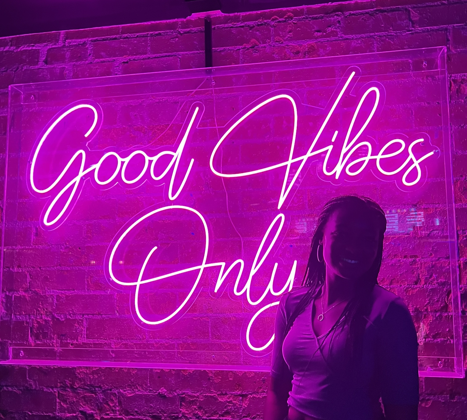Belinda by a lit sign that says, "Good Vibes Only."