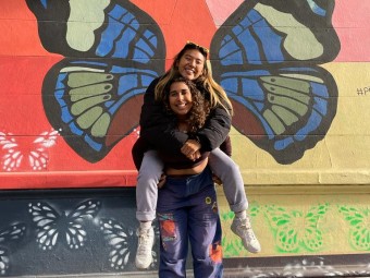 Anusha with a friend posing by a butterfly mural.