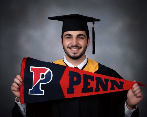 Photo of Maher Abdel Samad holding a Penn flag whilst wearing graduation regalia