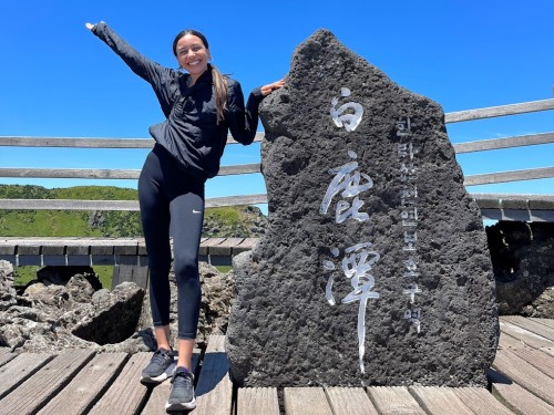 Student posing with engraved rock with Korean text on the Summit of Mountain Hallasan