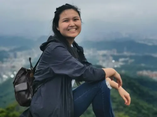 Smiling student sitting on a hill overlooking a city in the background