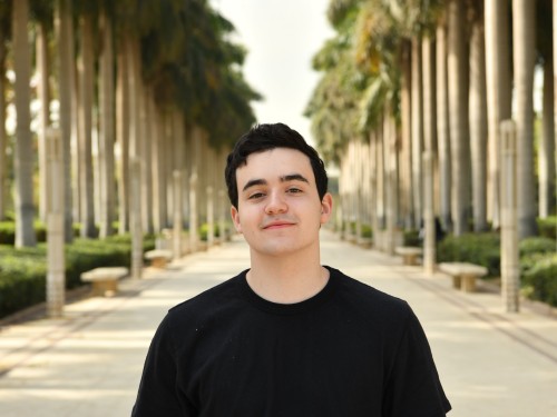 Portrait of Daniel standing in front of a row of palm trees