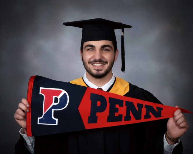 Maher Abdel Samad holding a Penn flag whilst wearing graduation regalia