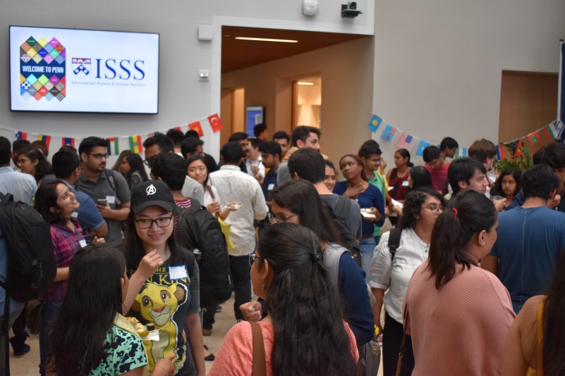 Students interacting with each other inside of Perry World House during 2019 international graduate student orientation. Flags of several countries are hung around the room.