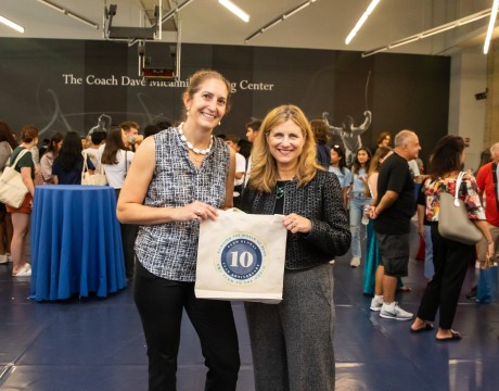 Penn President Liz Magill and Associate Vice Provost for Global Initiatives Amy Gadsden stand side-by-side holding a Penn Global 10th anniversary canvas tote. 