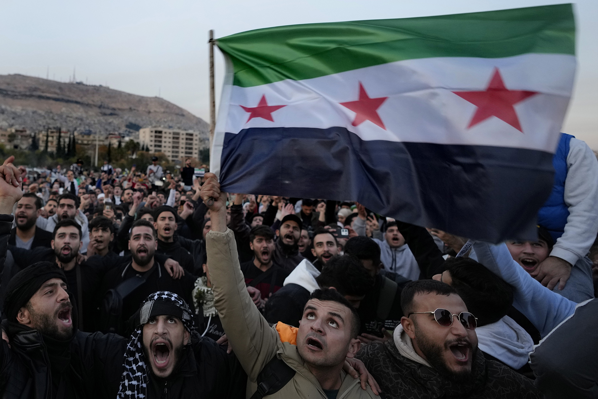 Syrian citizens wave the revolutionary flag as they celebrate the takeover of the capital Damascus by insurgents. (Image: AP Photo/Hussein Malla)